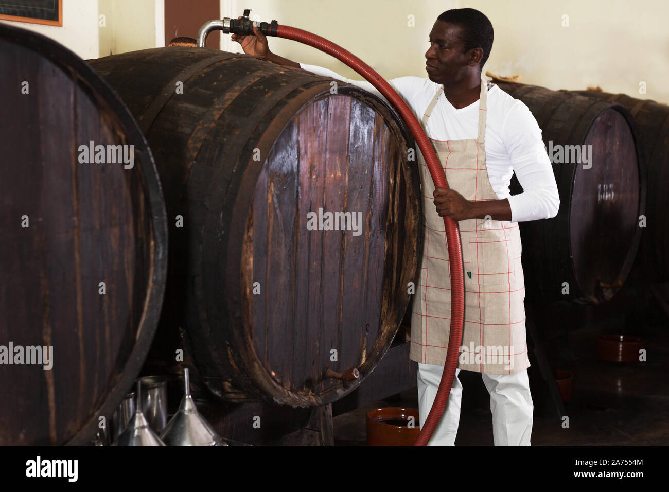 Confident man winemaker working in winevault, filtering wine in