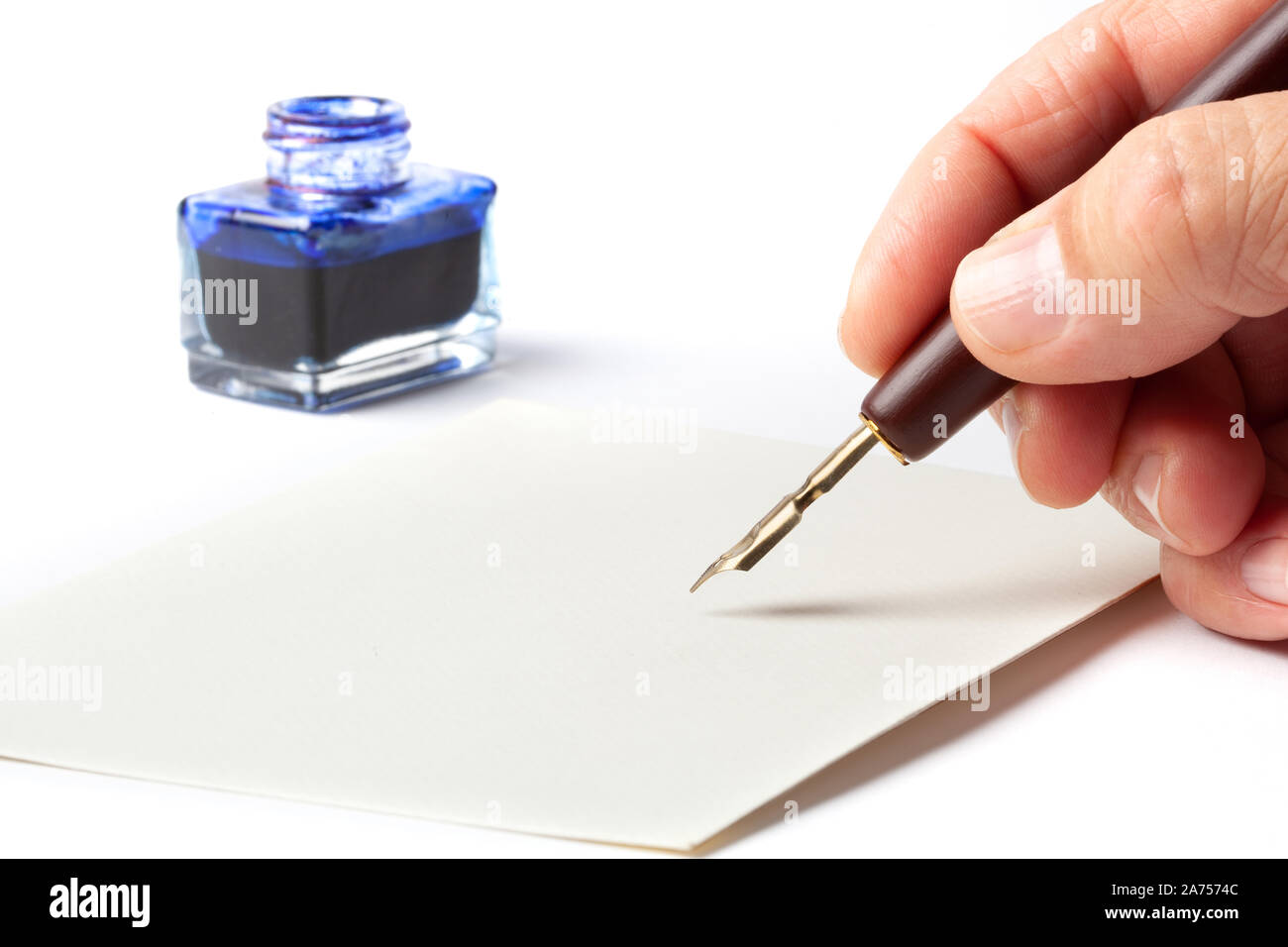 Hand with an old calligraphy fountain ink pen over a blank mail envelope isolated on white background. Stock Photo