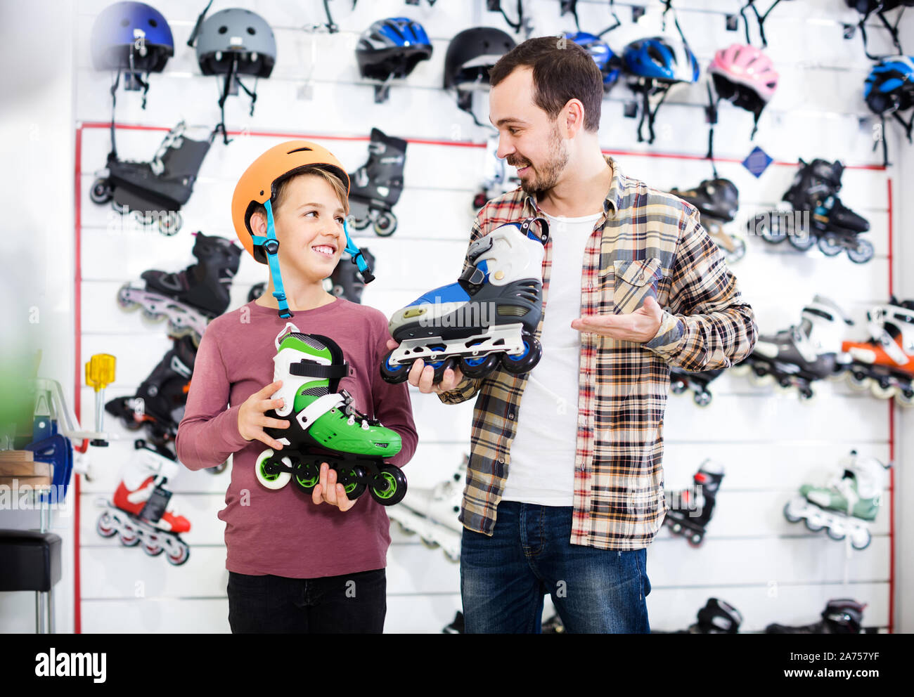 happy spanish male shop assistant helping boy to choose rollerskates