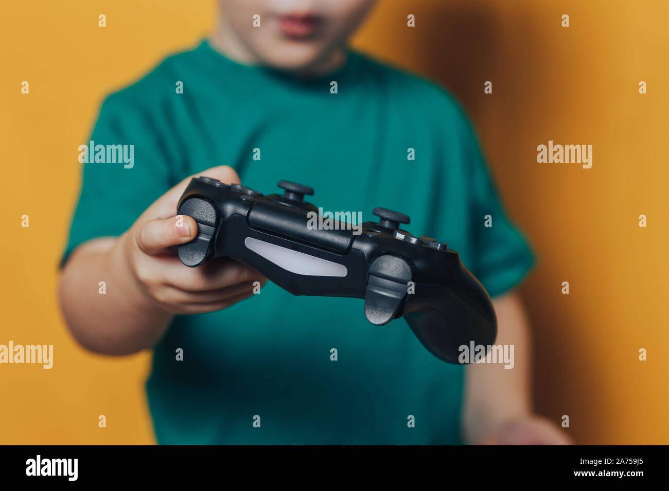 Little boy playing with black joystick have emotions on his face, he is surprisedon yellow background. Stock Photo