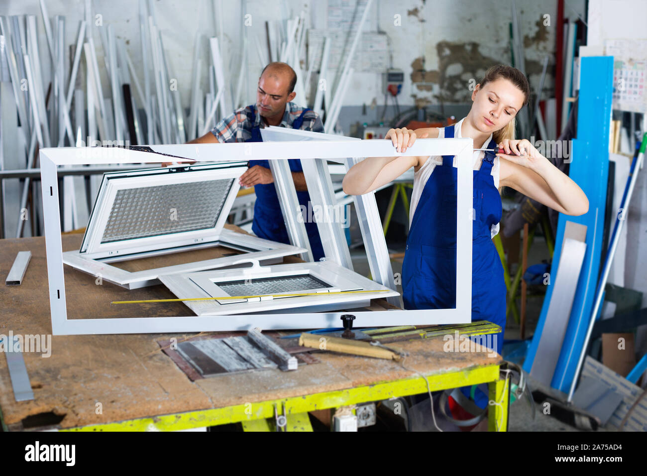 Efficient positive  workwoman assembling PVC window in workshop with manual tools Stock Photo