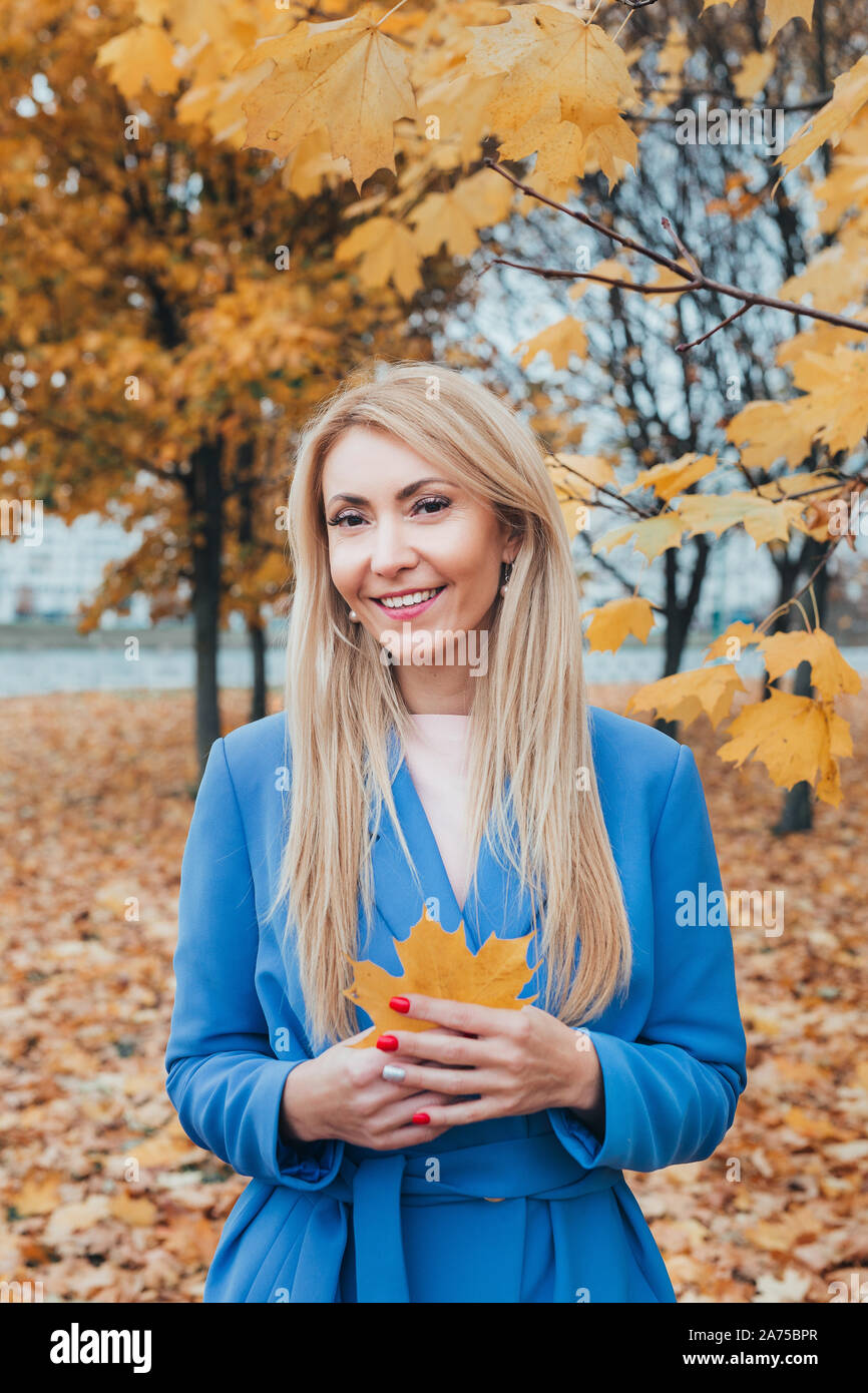 beautiful smiling mature woman with autumn maple leaves in hands in park Stock Photo