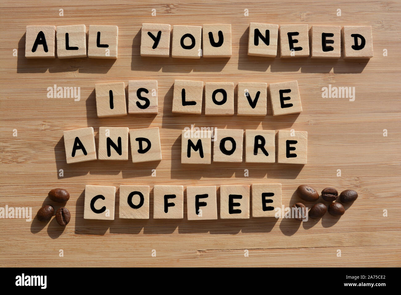 All You Need Is Love And More Coffee-. Words in 3d wooden alphabet letters with coffee beans on a bamboo wood background Stock Photo