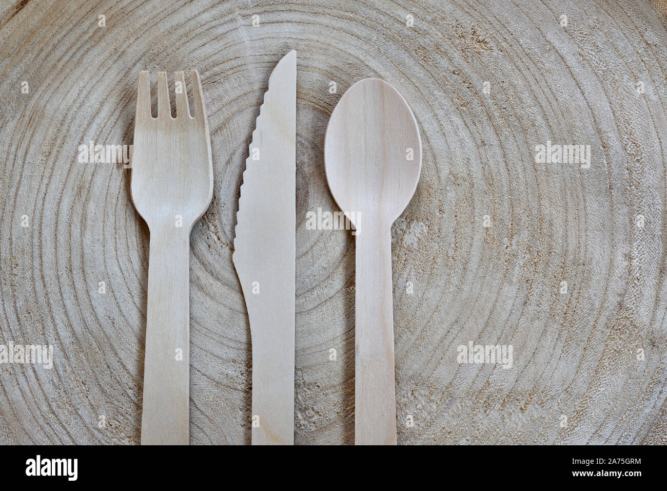 Plastic-free, disposable cutlery made of wood. Wooden fork, knife and spoon on a tree slice. Pro environmental concept, copy space for text and design Stock Photo