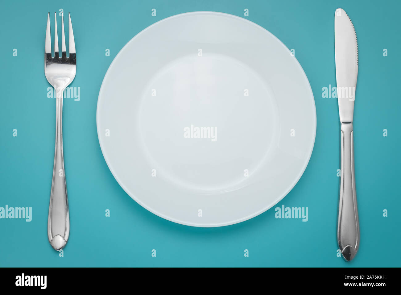 White empty plate with fork and knife on blue background. Turquoise backdrop. Laying, table appointments. Stock Photo
