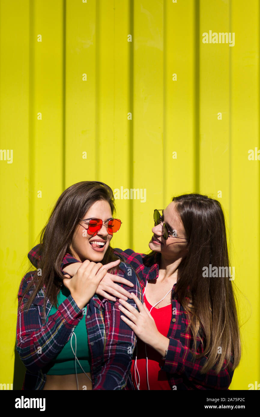 Image of two young happy women friends standing outdoor over yellow wall Stock Photo