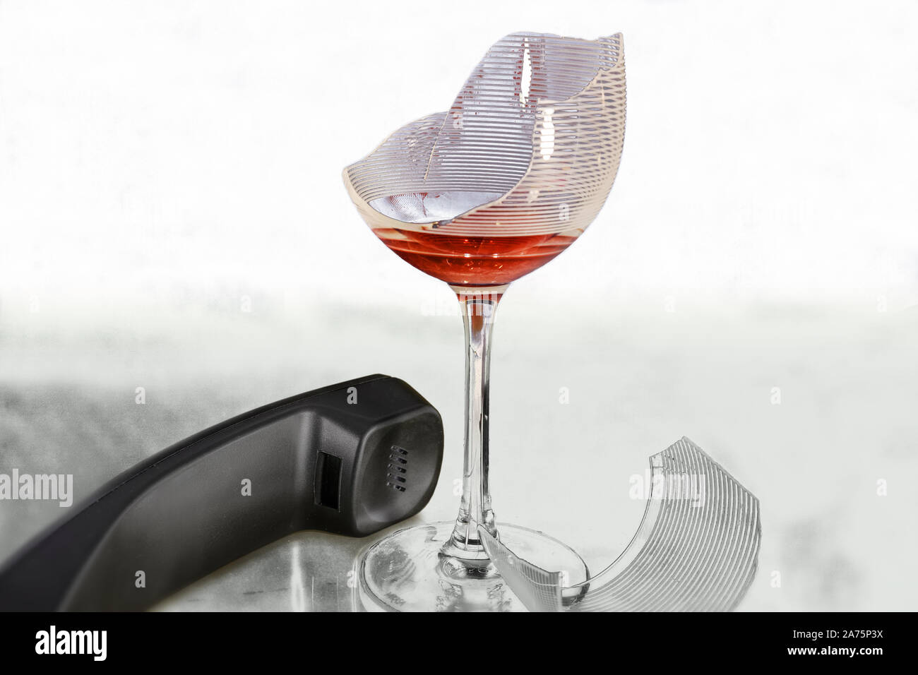 A broken wine glass and a phone receiver next to it. High key, high contrast and copy space. Stock Photo