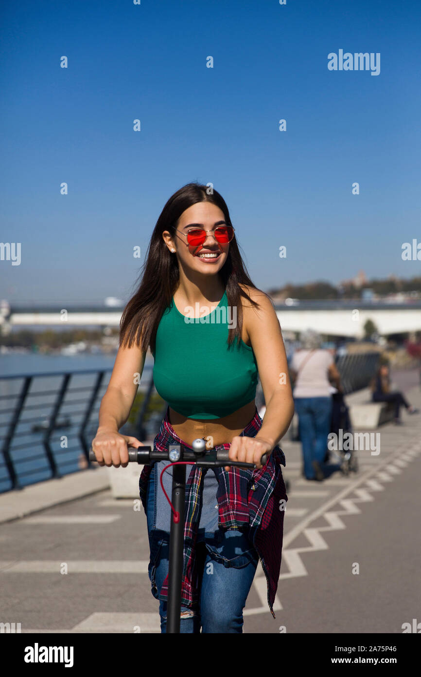 Pretty young woman riding an electric scooter in the street on a sunny day Stock Photo