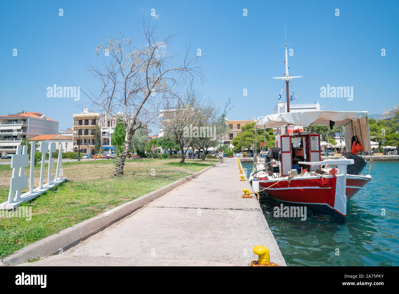 Waterfront with hashtad Itea on grass beside promenade with boat moored tied to yellow bollards. Stock Photo