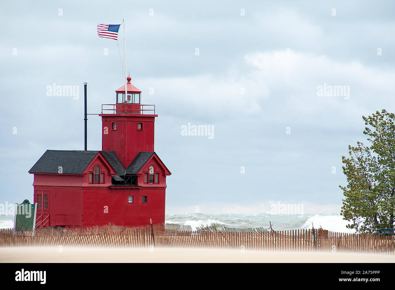 Red Michigan lighthouse on Lake Michigan with beach fence and high seas in wind storm Stock Photo