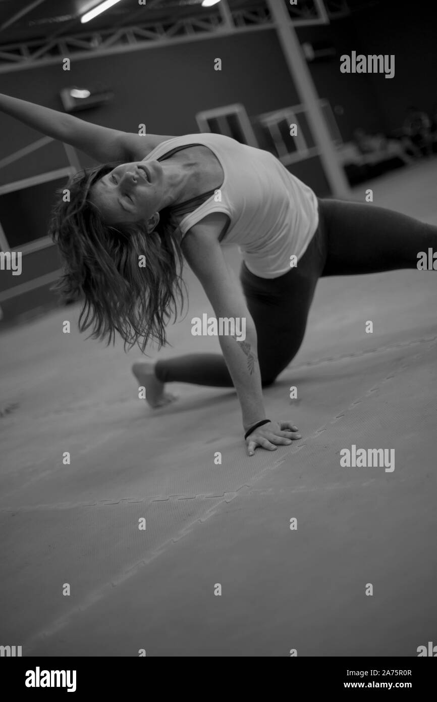 Young beautiful woman practicing yoga with gym view in the background. Monochromatic picture. New year, new you! Stock Photo