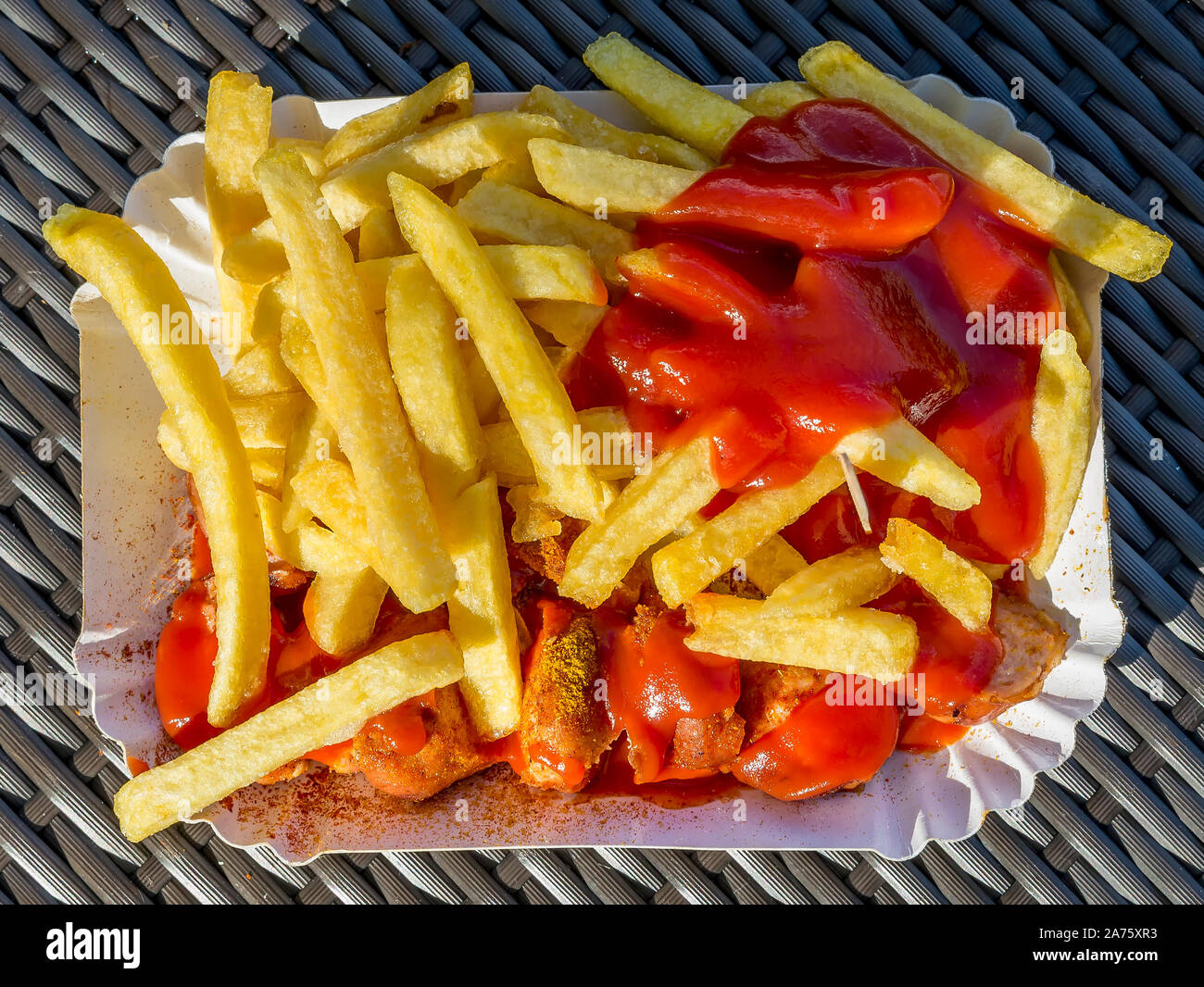 Delicious cardboard plate filled with ketchup-coated fries accompanied by currywurst, a German culinary specialty, to eat outdoors Stock Photo