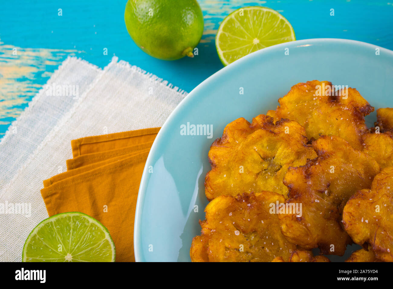 Food photography of a blue plate with deep fried plantains Latin American tostones or patacones with limes. Stock Photo