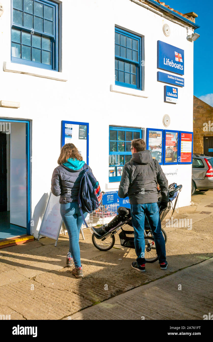 A family outside the RNLI charity shop below the cliff at Cow Bar Nab  Staithes North Yorkshire Stock Photo