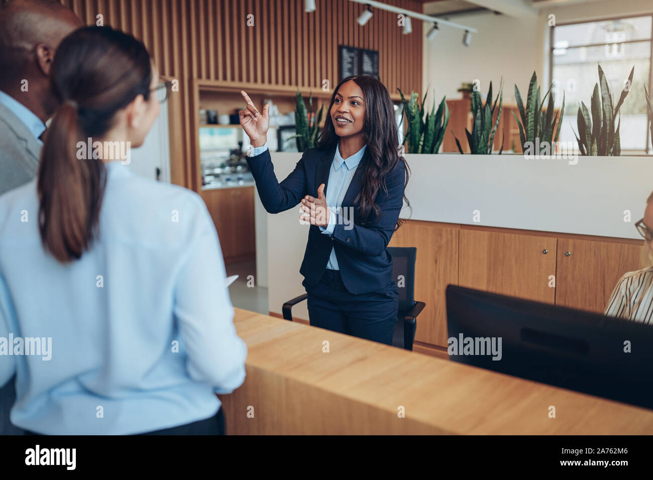 Smiling young African American concierge giving two guests directions to their room while checking them into her hotel Stock Photo