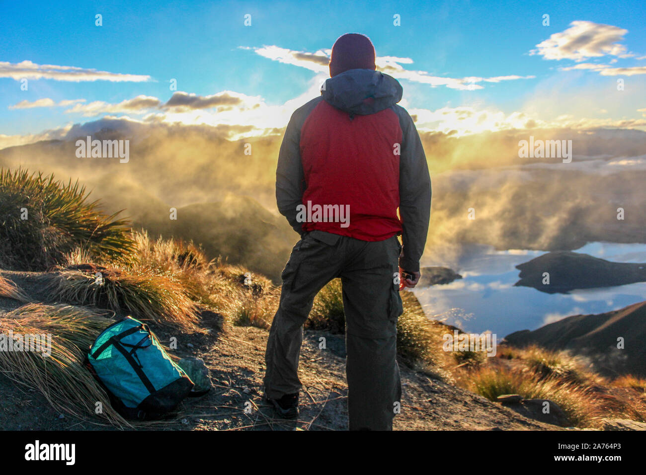 Man in rain gear looking out towards clouds on top of mountain in NZ. Stock Photo