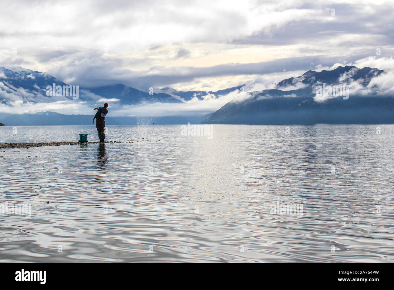 Man skipping rock in New Zealand with mountains in the background. Stock Photo