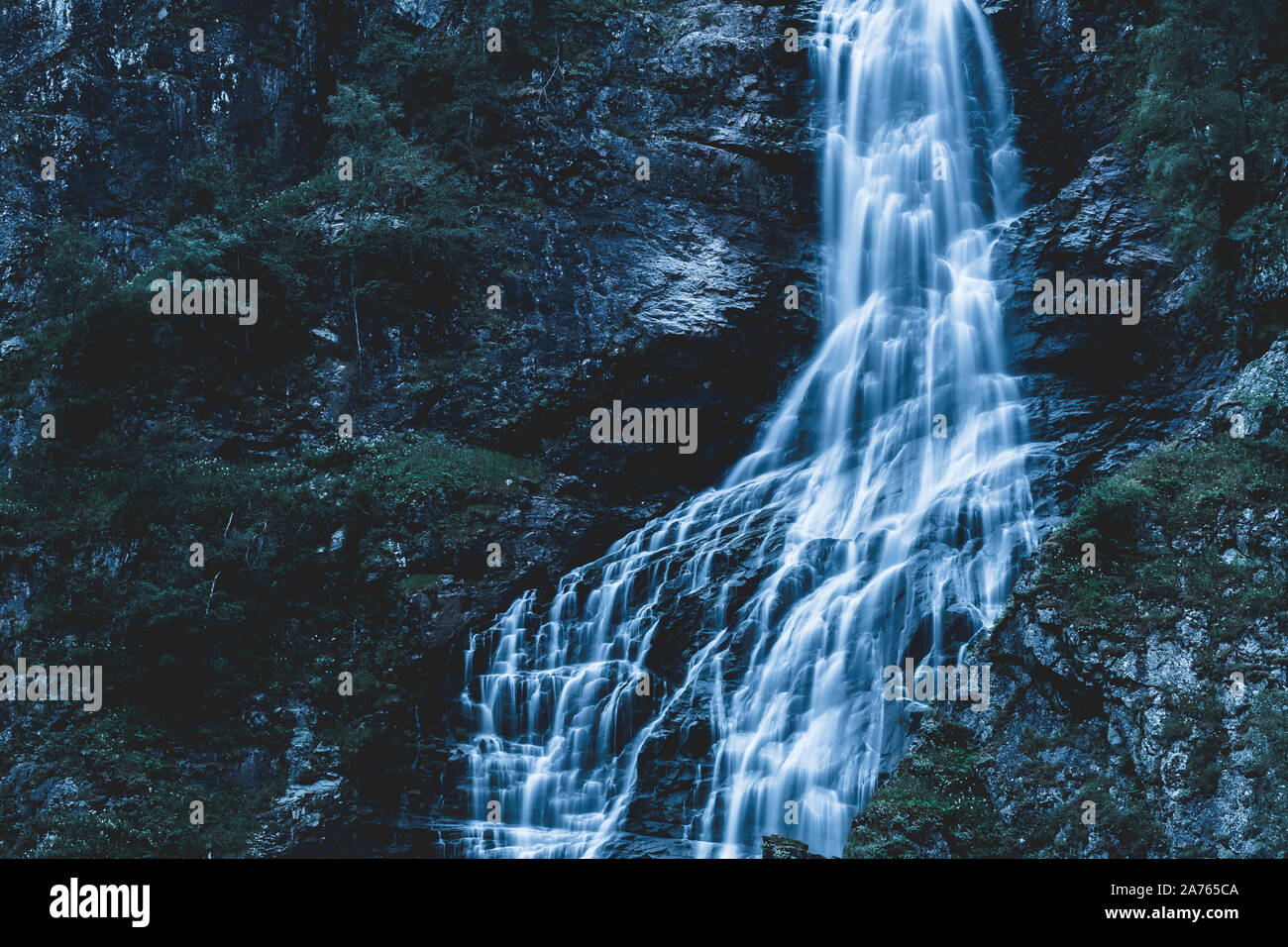 Glowing waterfall on a rocky mountainside covered in green bushes Stock Photo