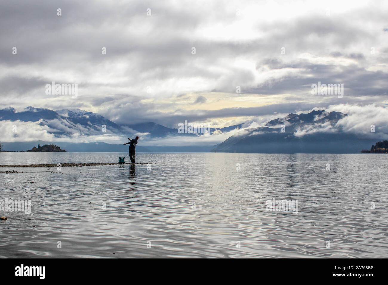 Man throwing rock into lake overlooking stunning New Zealand mountains Stock Photo