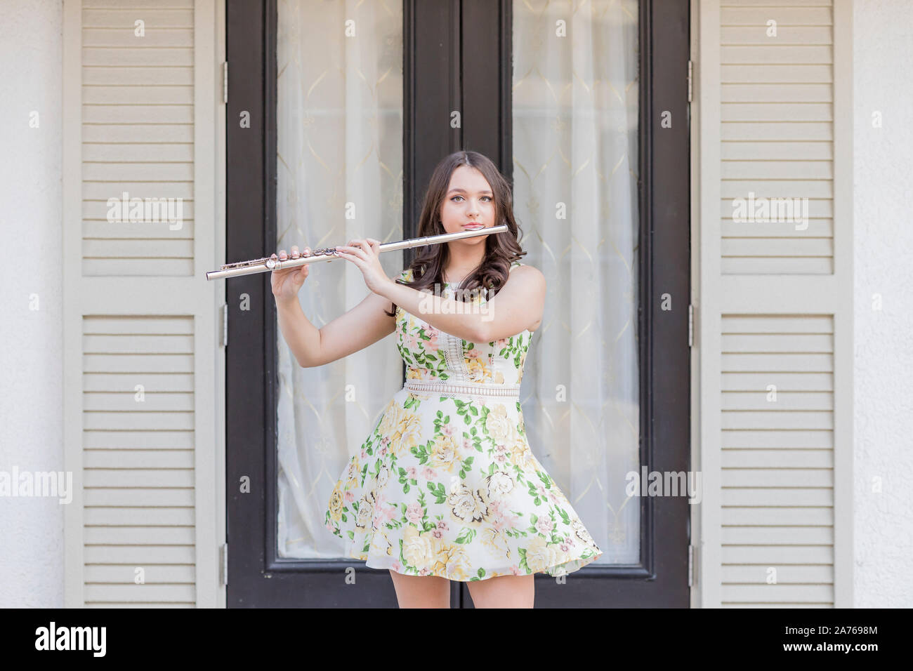 Girl in floral dress plays flute on the street on a windy day Stock Photo
