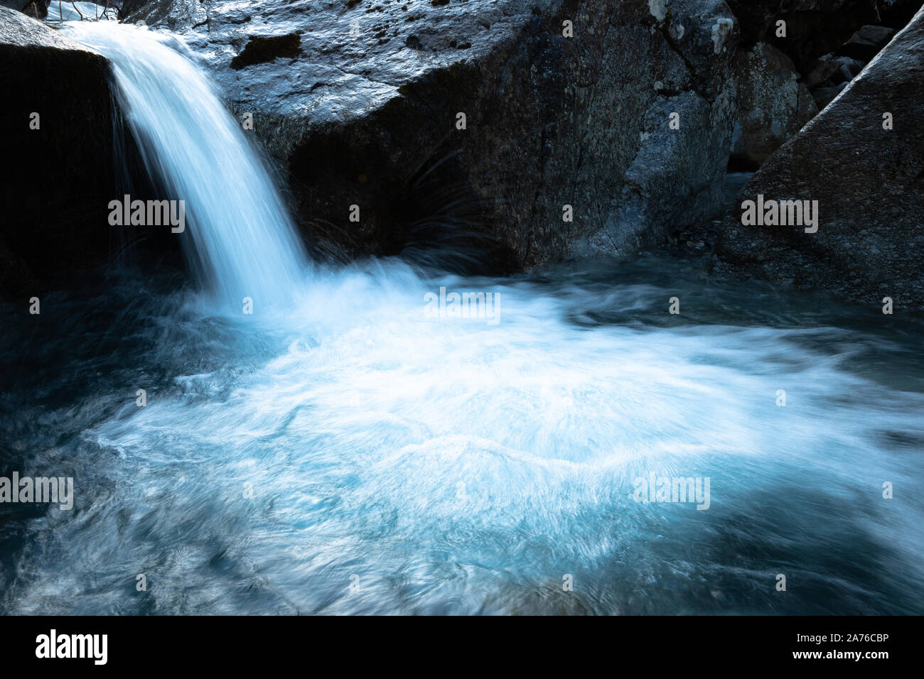 An Apine waterfall with blue water against dark rock Stock Photo