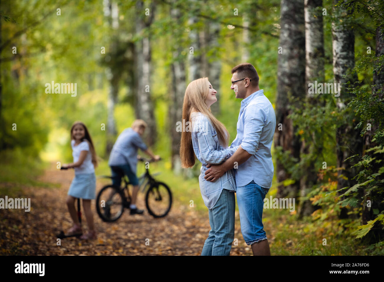 Children having fun while parents kisses. Family on outdoor walk in the park in summer. Stock Photo