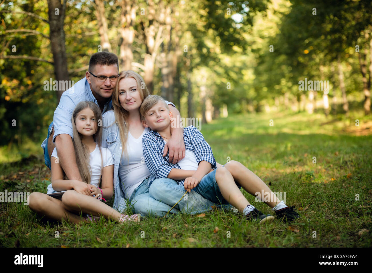 Happy family of four sitting on a grass in summer park outdoors and smiling Stock Photo