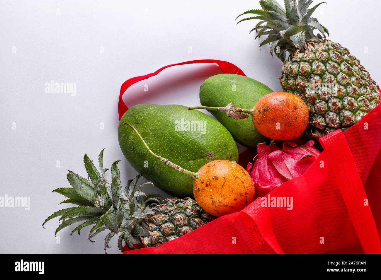 Zero waste concept, Red shopping textile bag with fresh tropical fruits: mango, pineapple, dragon and passion fruit on white background Stock Photo