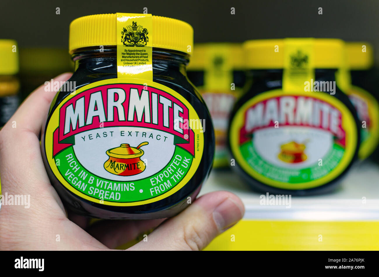 Marmite jar hold in a hand next to supermarket shelf with the other jars. Traditional English product made of yeast. Stock Photo