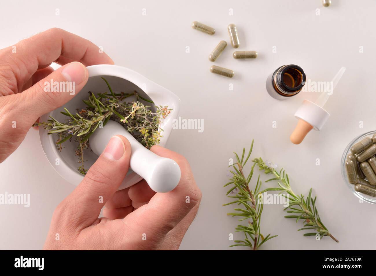 Hands elaborating alternative medicine with plants with mortar on white table. Alternative natural medicine concept. Top view. Horizontal composition. Stock Photo