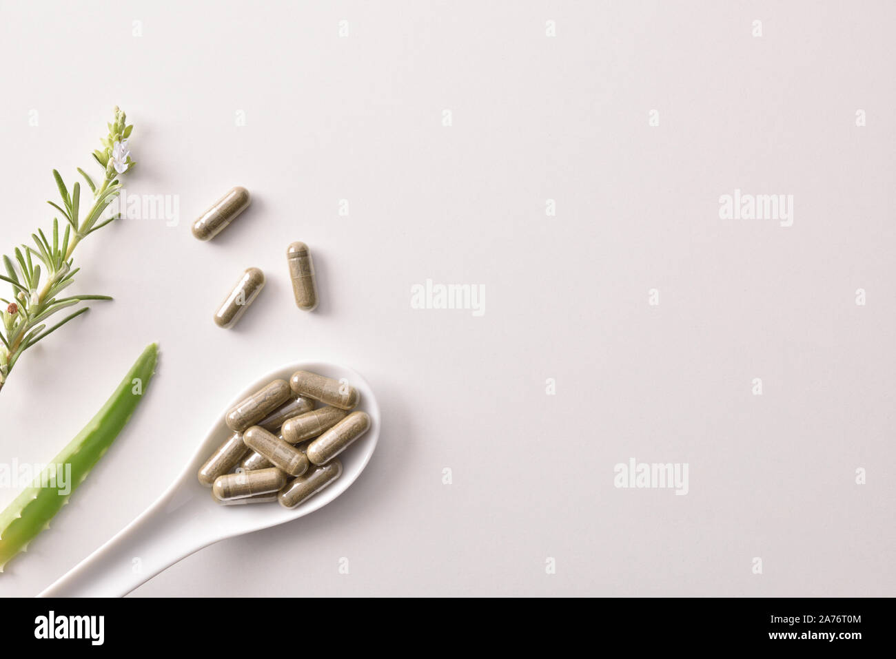 Background with capsules of natural medicine on a ceramic spoon and rosemary and aloe vera on white table. Top view. Horizontal composition. Stock Photo