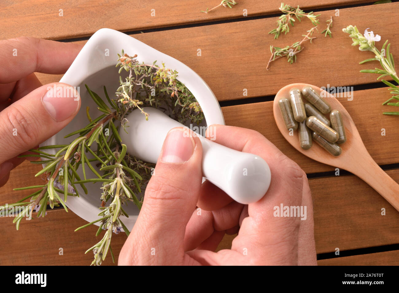 Hands making homemade natural medicines in a white ceramic mortar with wooden spoon with capsules and plants. Alternative natural medicine concept. To Stock Photo