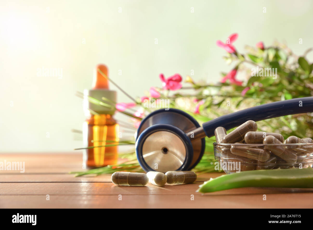 Natural herbal medicine capsules on wood table with stethoscope plants and bottle with medicinal liquid and green background. Alternative natural medi Stock Photo