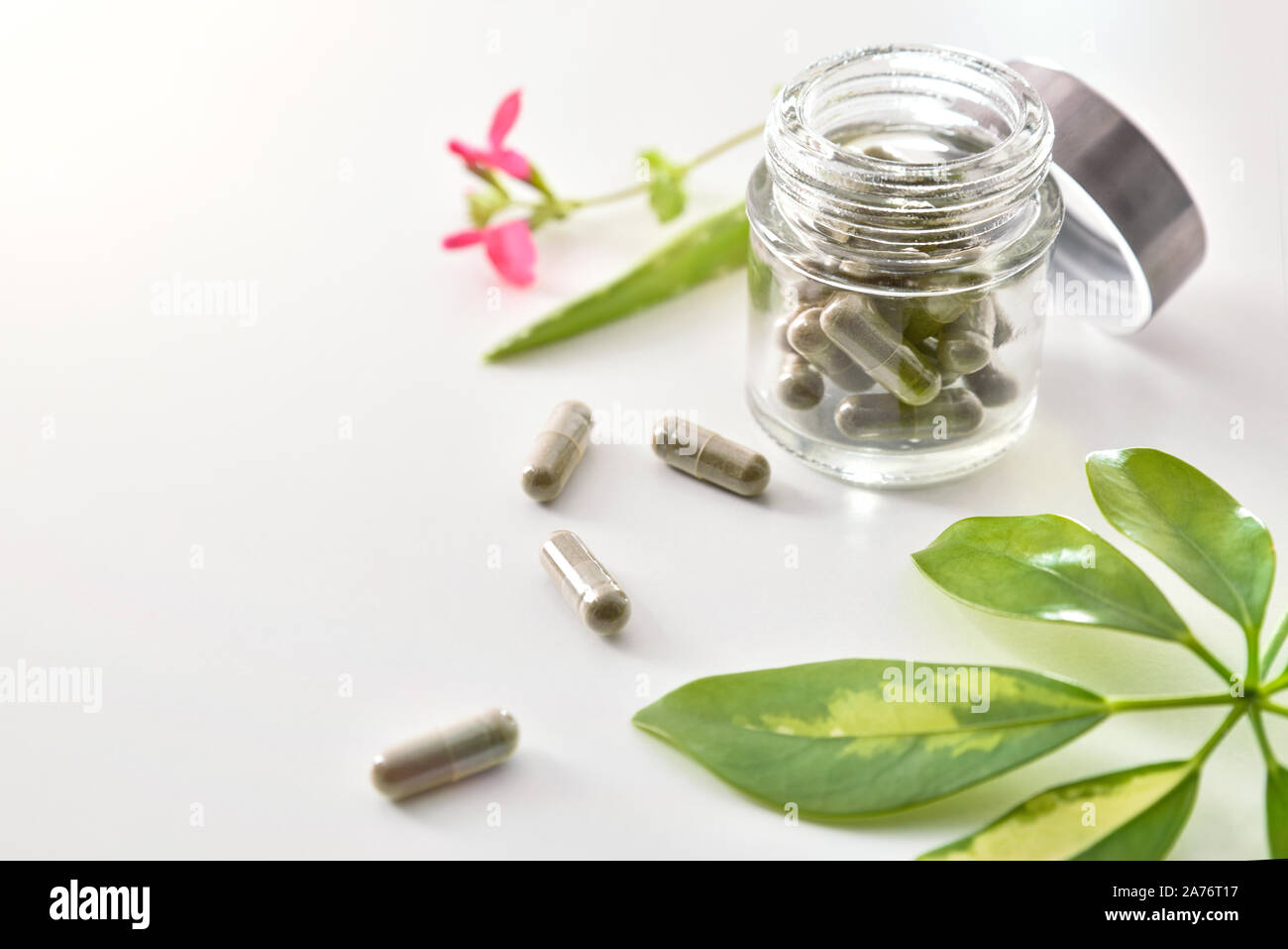 Natural medicine capsules in open glass jar lying on white table with aloe vera and plant leaves. Natural medicine concept. Elevated view. Horizontal Stock Photo