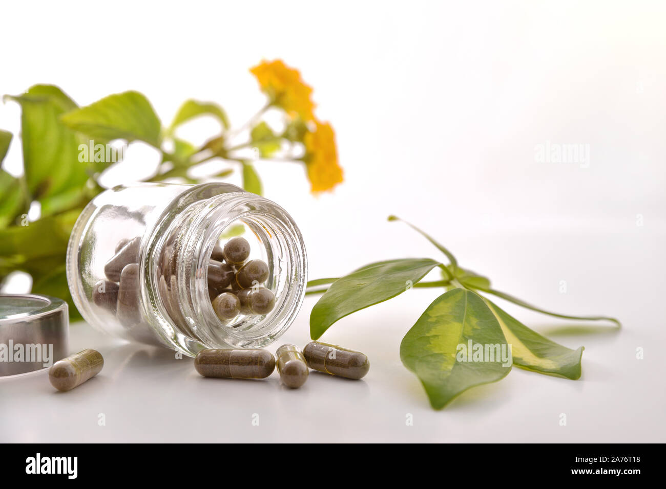 Natural medicine capsules in open glass jar lying on white table with aloe vera and plant leaves. Natural medicine concept. Front view. Horizontal com Stock Photo
