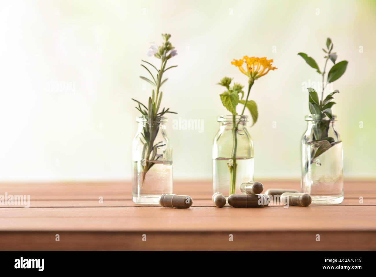 Natural herbal medicine capsules on wooden table with tree bottles with liquid and plants behind and green background. Alternative natural medicine co Stock Photo