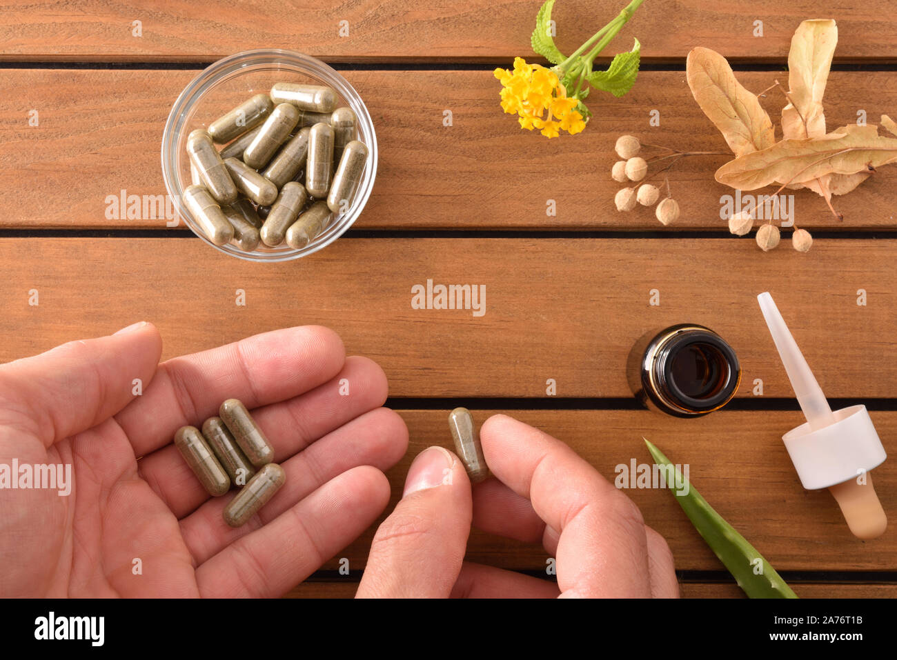 Hands taking natural medicine capsules of herbs on wooden table with glass container with plant capsules and dropper bottle with medicinal liquid. Alt Stock Photo