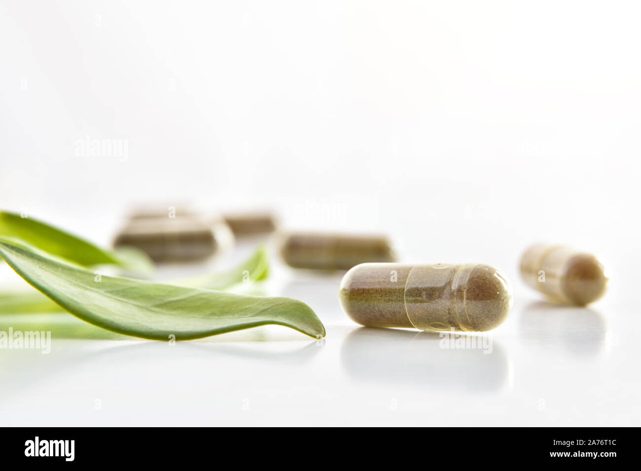 Natural medicine capsules and plant leaf on white table isolated white. Natural medicine concept. Front view. Horizontal composition. Stock Photo