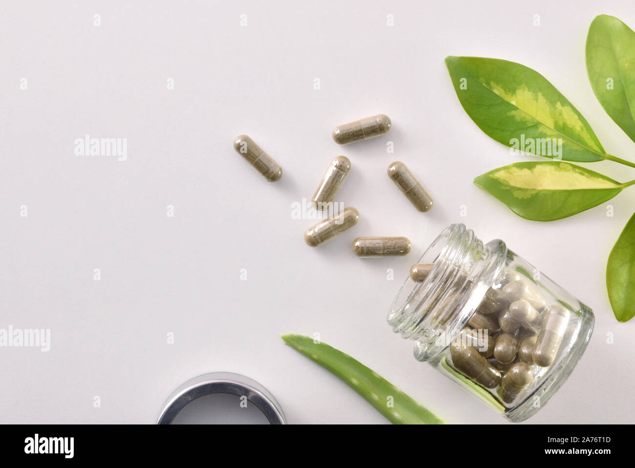 Natural medicine capsules in open glass jar lying on white table with aloe vera and plant leaves. Natural medicine concept. Top view. Horizontal compo Stock Photo