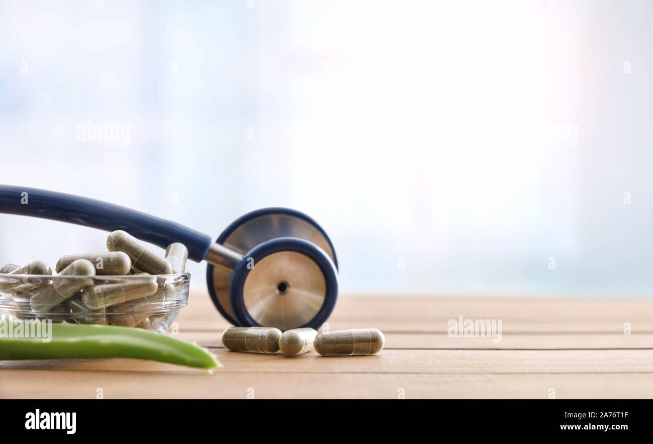 Natural herbal medicine capsules with stethoscope and aloe vera on wood table and blue background. Alternative natural medicine concept. Front view. H Stock Photo