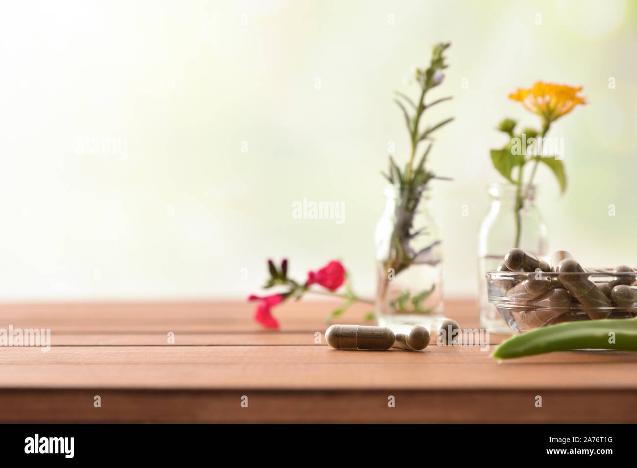 Natural herbal medicine capsules on wooden table with two bottles with liquid and plants behind and green background. Alternative natural medicine con Stock Photo