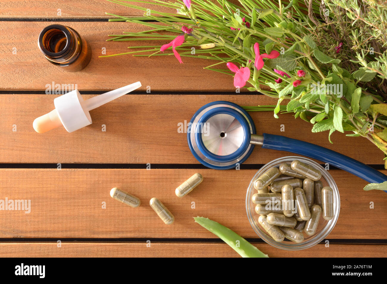 Natural herbal medicine capsules on wood table with stethoscope plants and dropper bottle with medicinal liquid. Alternative natural medicine concept. Stock Photo