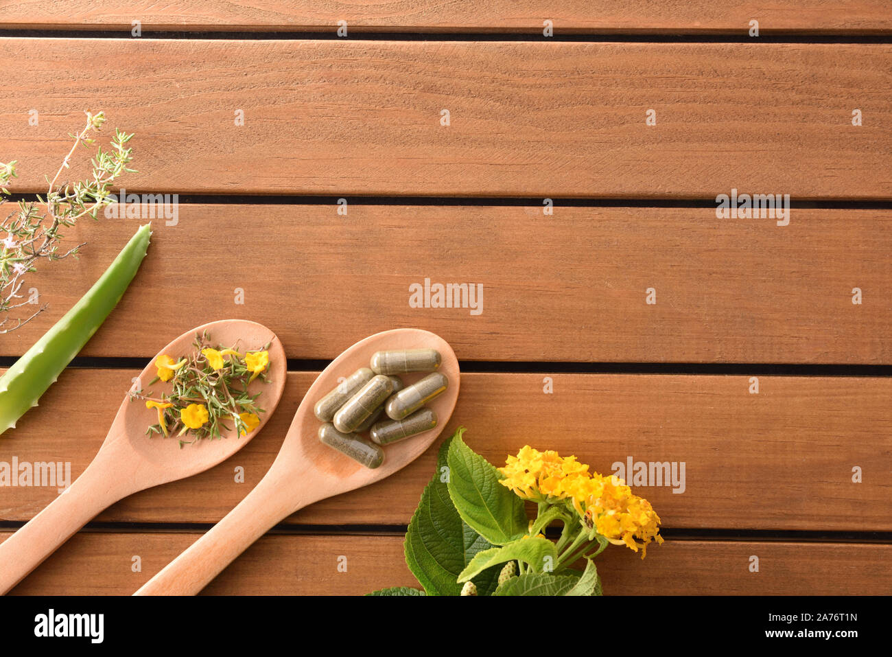 Natural medicine capsules of herbs on wood spoon on wooden table with plant. Alternative natural medicine concept. Top view. Horizontal composition. Stock Photo