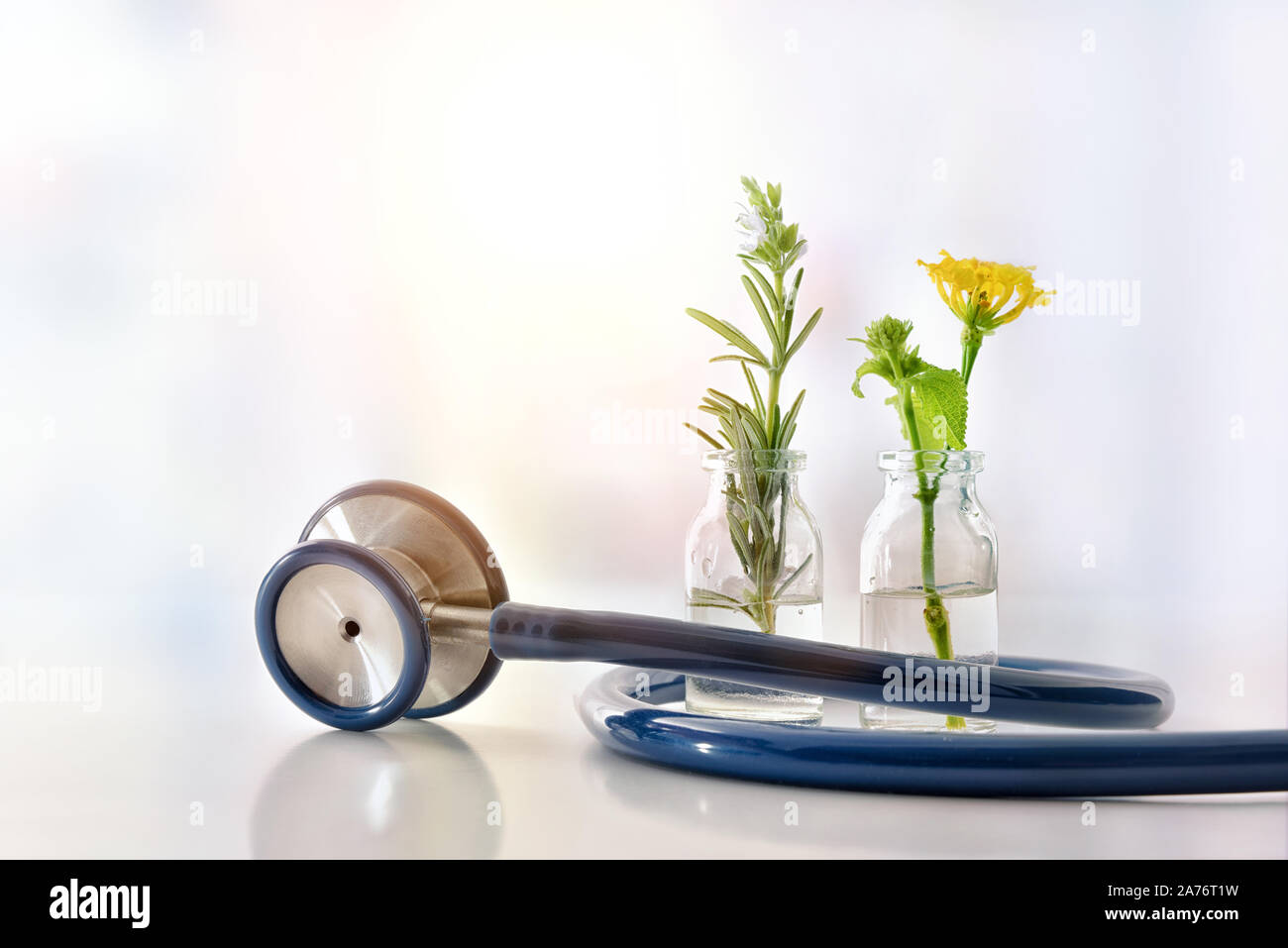 Two bottles with plant essence liquid with plants inside and blue stethoscope on white table. Alternative natural medicine concept. Front view. Horizo Stock Photo