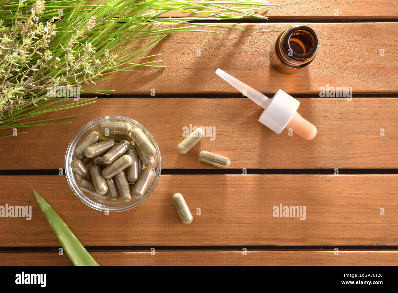 Natural herbal medicine capsules on wood table with plants and dropper bottle with medicinal liquid. Alternative natural medicine concept. Top view. H Stock Photo
