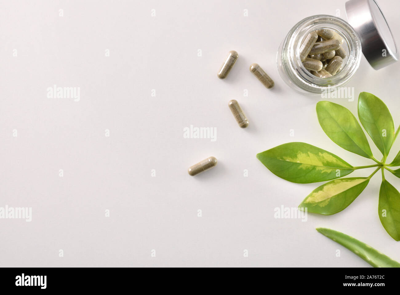 Natural medicine capsules in open glass jar on white table with aloe vera and plant leaves. Natural medicine concept. Top view. Horizontal composition Stock Photo