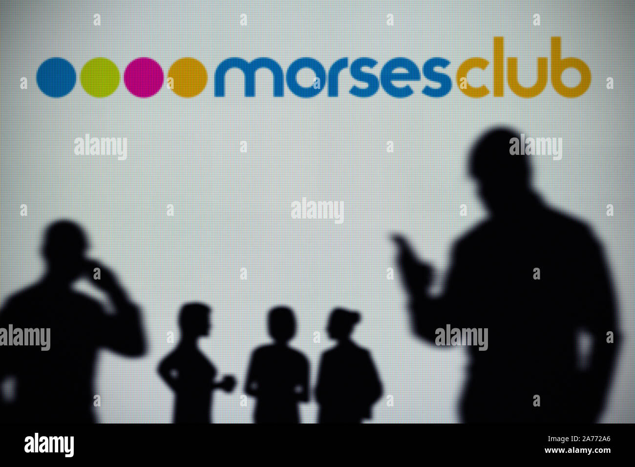 The Morses Club logo is seen on an LED screen in the background while a silhouetted person uses a smartphone (Editorial use only) Stock Photo