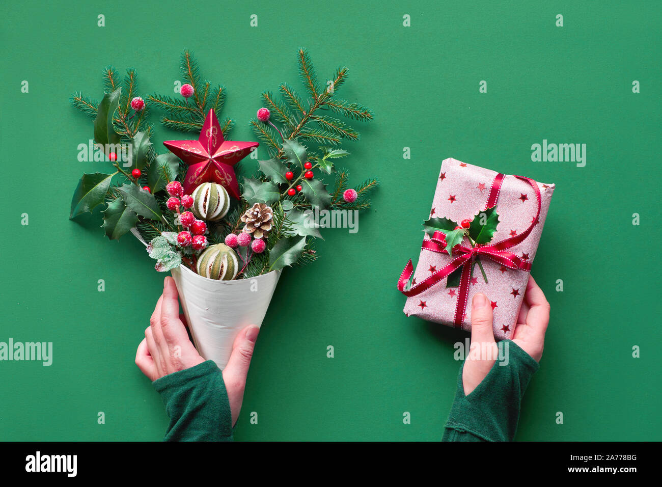 Christmas background flat lay on green paper. Female hand holding veneer cone with fir and holly twigs decorated with candy canes and berries. Another Stock Photo