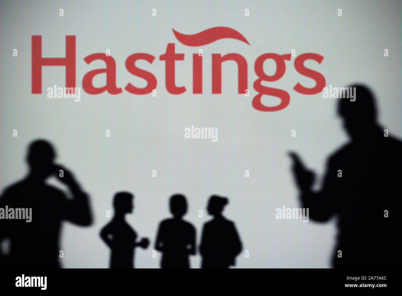 The Hastings Group logo is seen on an LED screen in the background while a silhouetted person uses a smartphone (Editorial use only) Stock Photo