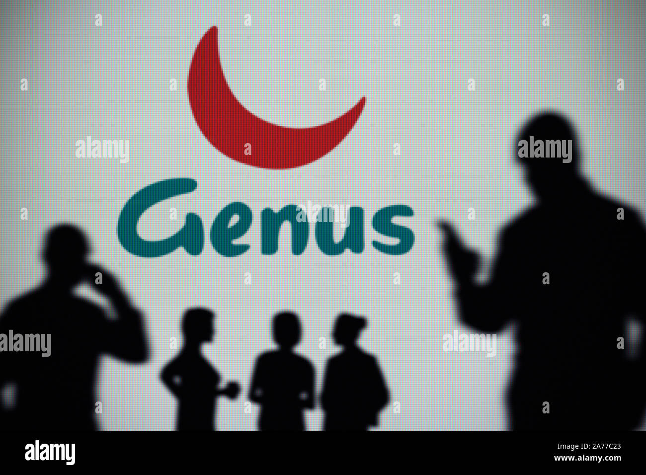 The Genus plc logo is seen on an LED screen in the background while a silhouetted person uses a smartphone (Editorial use only) Stock Photo